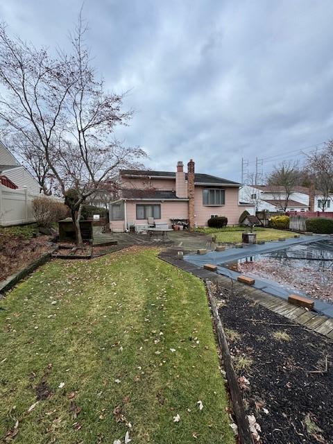 rear view of house featuring a yard, a chimney, and fence