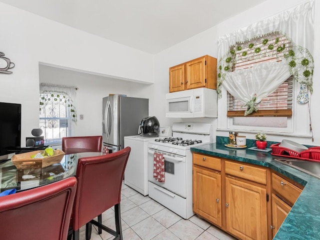 kitchen featuring dark countertops, white appliances, brown cabinetry, and light tile patterned flooring