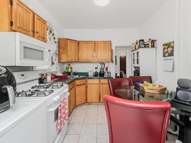 kitchen with light tile patterned flooring, white appliances, a sink, a center island, and dark countertops