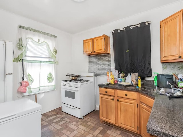 kitchen featuring refrigerator, tasteful backsplash, dark countertops, a sink, and white gas range oven