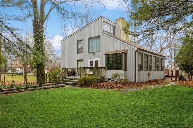 back of house featuring a chimney, a lawn, and a wooden deck