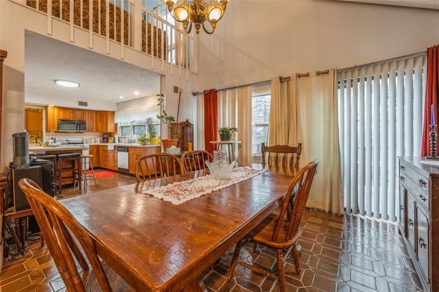 dining space with a healthy amount of sunlight, an inviting chandelier, dark tile patterned floors, and a high ceiling