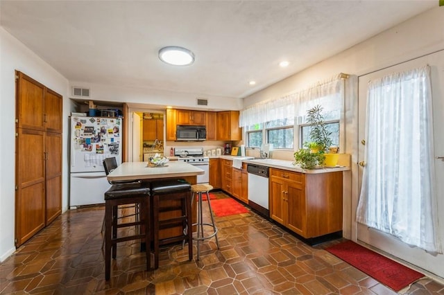 kitchen featuring white appliances, a breakfast bar, visible vents, light countertops, and brown cabinetry