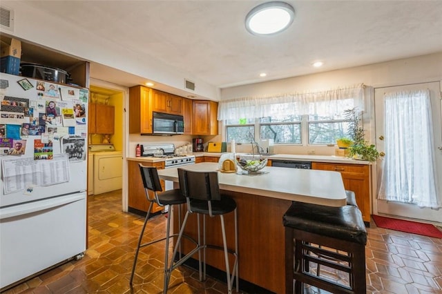 kitchen featuring white appliances, brown cabinetry, washer / clothes dryer, light countertops, and a kitchen bar