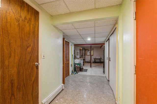 hall with a paneled ceiling, a baseboard radiator, baseboards, and tile patterned floors