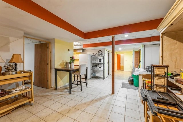 interior space with light tile patterned floors, a drop ceiling, freestanding refrigerator, and recessed lighting