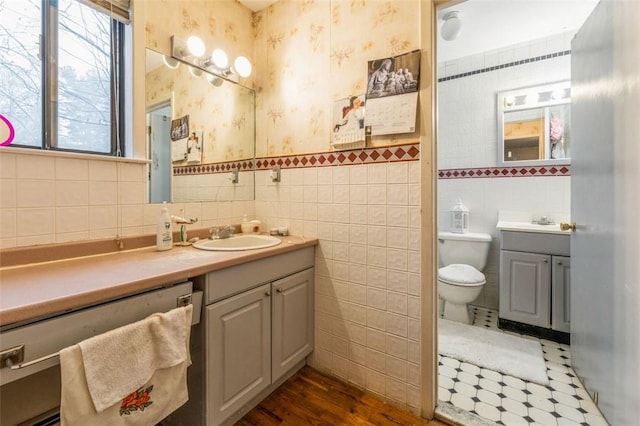 bathroom featuring vanity, tile walls, toilet, and wallpapered walls