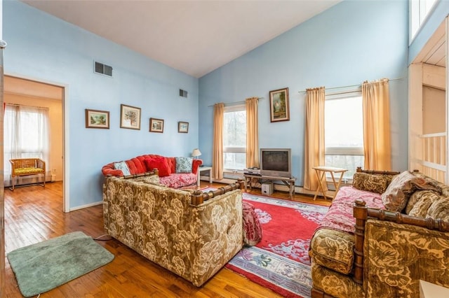 living room featuring high vaulted ceiling, visible vents, baseboards, and hardwood / wood-style flooring