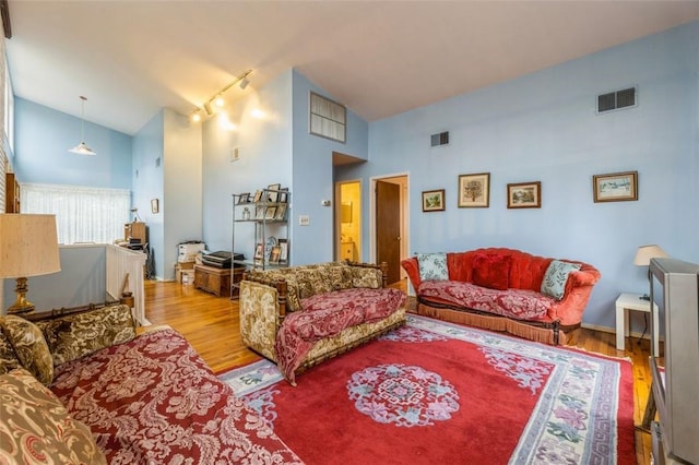 living room with high vaulted ceiling, rail lighting, visible vents, and wood finished floors