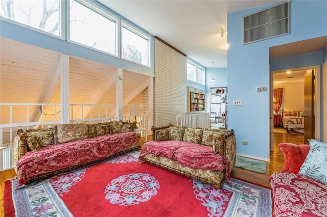 living area with a towering ceiling, wood finished floors, visible vents, and baseboards