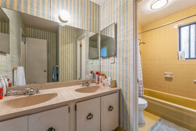 bathroom featuring toilet, wallpapered walls, double vanity, and a sink