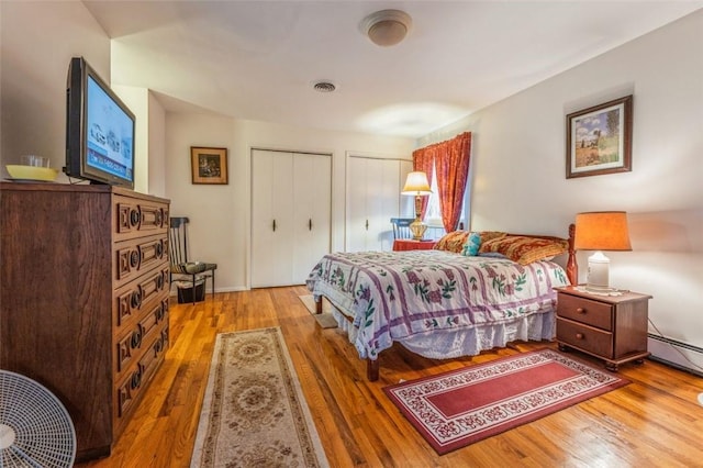 bedroom with wood finished floors, visible vents, baseboard heating, and two closets