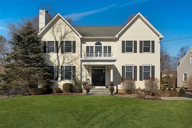 view of front facade featuring a front lawn, a chimney, and a balcony