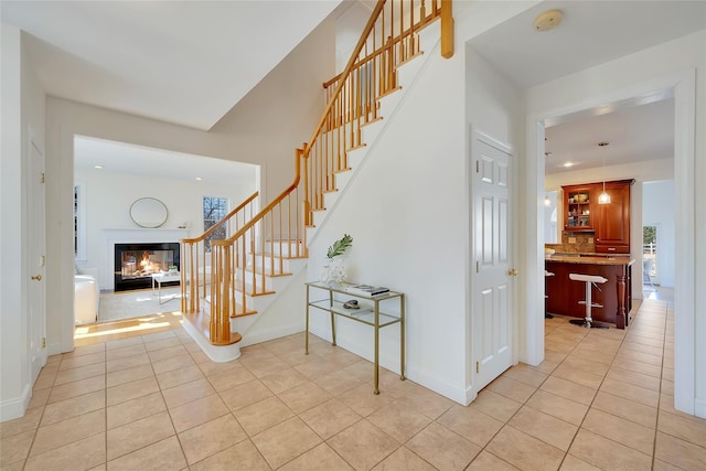 foyer entrance with stairs, light tile patterned flooring, a multi sided fireplace, and baseboards