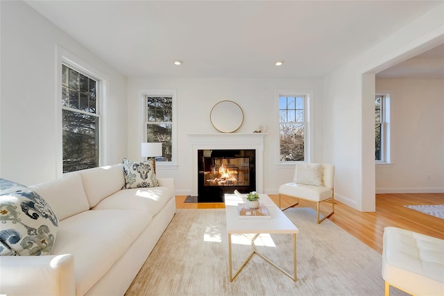 living room featuring a fireplace with flush hearth, baseboards, wood finished floors, and recessed lighting