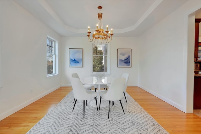 dining area featuring light wood-style floors, a tray ceiling, a chandelier, and a healthy amount of sunlight