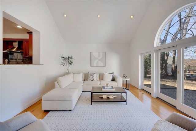 living room with high vaulted ceiling, light wood-style flooring, and baseboards