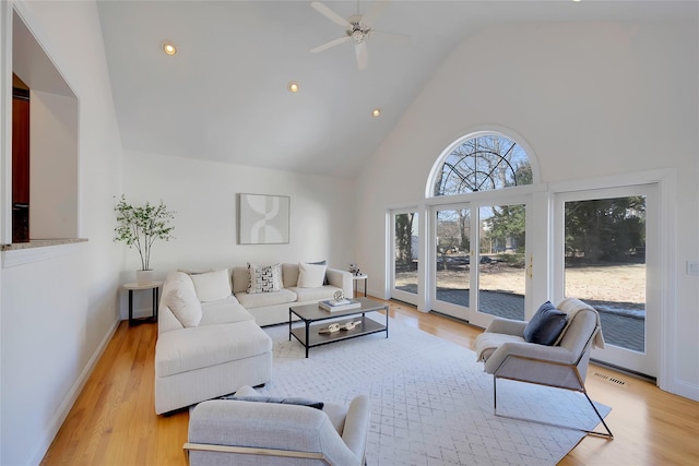 living room with high vaulted ceiling, light wood-type flooring, visible vents, and baseboards