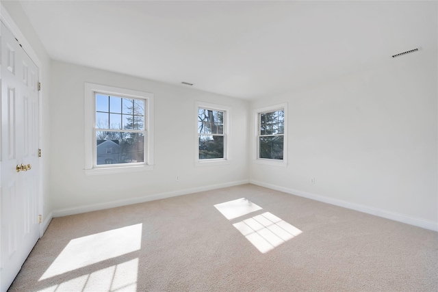 empty room featuring light carpet, plenty of natural light, and baseboards