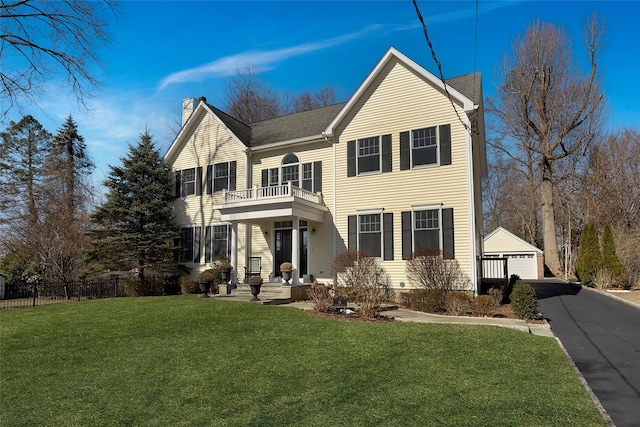 traditional home with a garage, a balcony, fence, an outdoor structure, and a front yard