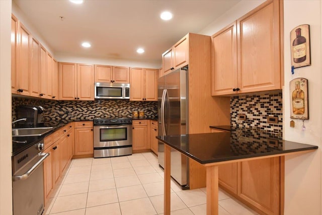 kitchen with light brown cabinetry, a kitchen breakfast bar, dark countertops, appliances with stainless steel finishes, and a peninsula