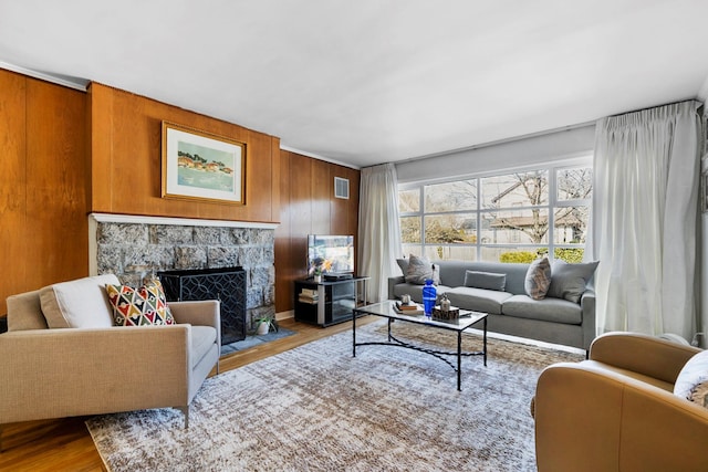 living area with a fireplace, wood finished floors, visible vents, and wooden walls