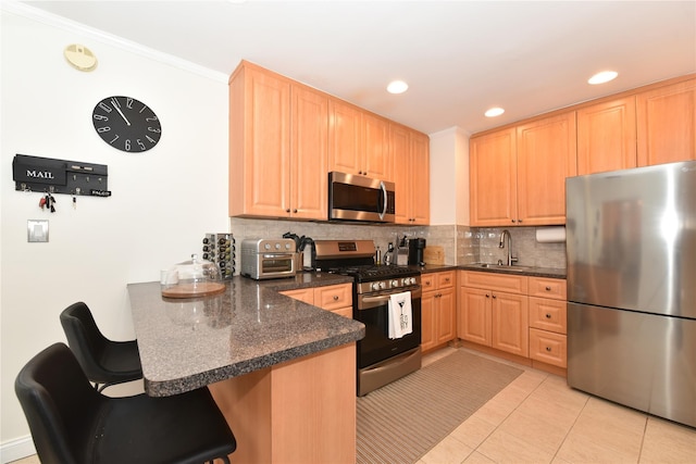 kitchen featuring a peninsula, appliances with stainless steel finishes, a sink, and light brown cabinetry