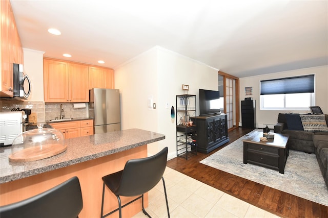 kitchen with appliances with stainless steel finishes, open floor plan, a sink, light brown cabinets, and backsplash