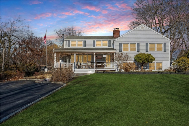 rear view of property with covered porch, a lawn, and a chimney