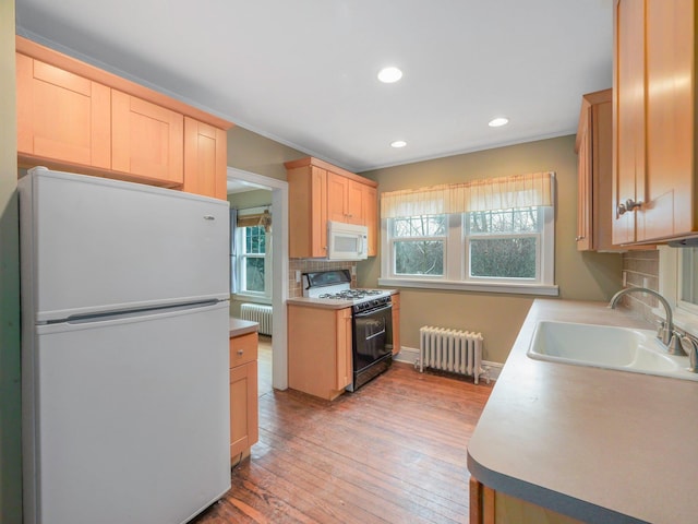 kitchen with white appliances, radiator heating unit, light brown cabinets, and a sink