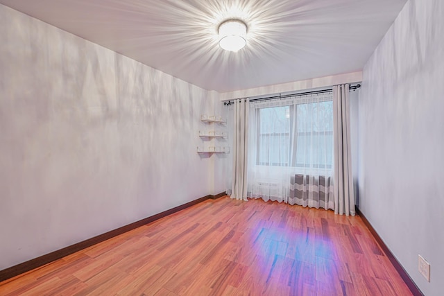 spare room with baseboards and wood finished floors