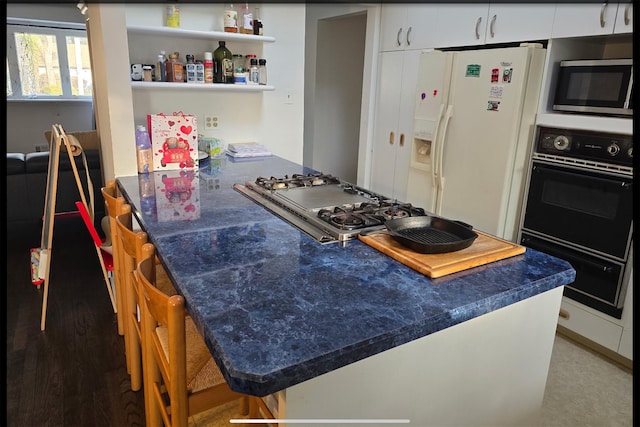 kitchen with a peninsula, a breakfast bar, white cabinetry, appliances with stainless steel finishes, and dark countertops