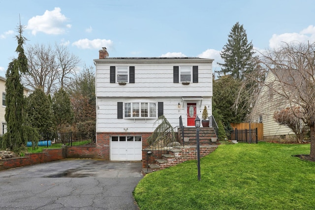 colonial house featuring fence, aphalt driveway, a front yard, a chimney, and an attached garage