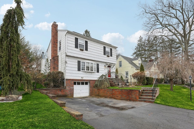 colonial-style house with a chimney, a front lawn, a garage, aphalt driveway, and brick siding