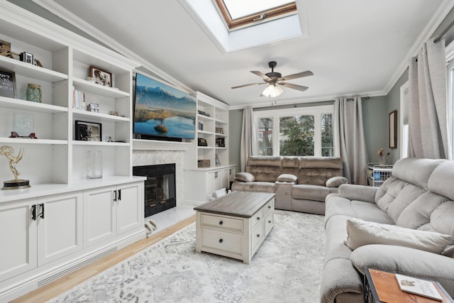 living area with light wood finished floors, ceiling fan, ornamental molding, a premium fireplace, and a skylight