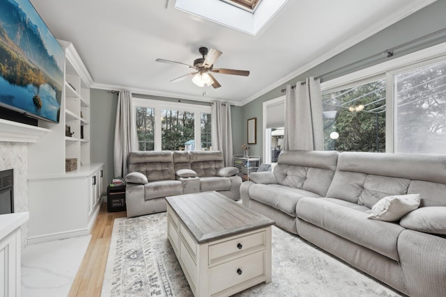 living area with crown molding, light wood-style flooring, a fireplace, a skylight, and a ceiling fan