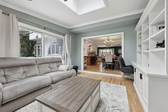 living area with light wood-style flooring, ornamental molding, an inviting chandelier, a skylight, and baseboards