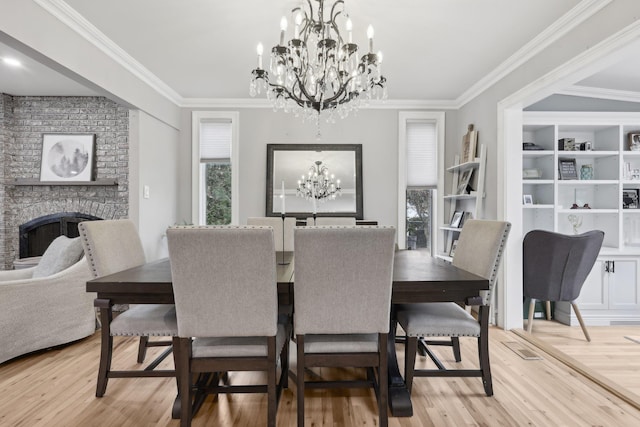 dining area with built in shelves, a large fireplace, ornamental molding, light wood-style floors, and an inviting chandelier