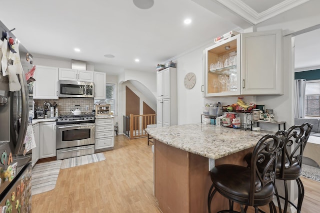 kitchen featuring a breakfast bar, ornamental molding, a peninsula, light wood-style floors, and stainless steel appliances