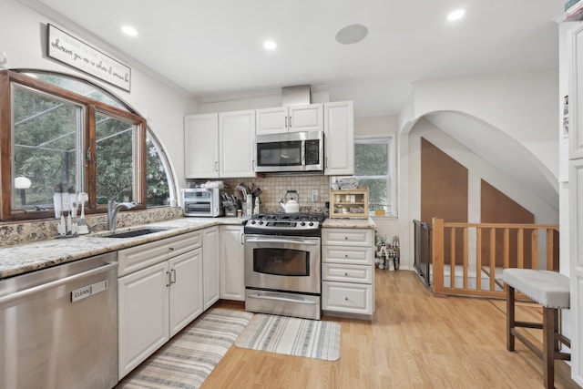 kitchen featuring light wood-type flooring, a sink, appliances with stainless steel finishes, white cabinets, and decorative backsplash