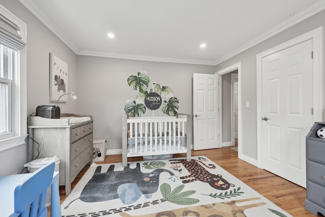 bedroom with a nursery area, ornamental molding, baseboards, and wood finished floors