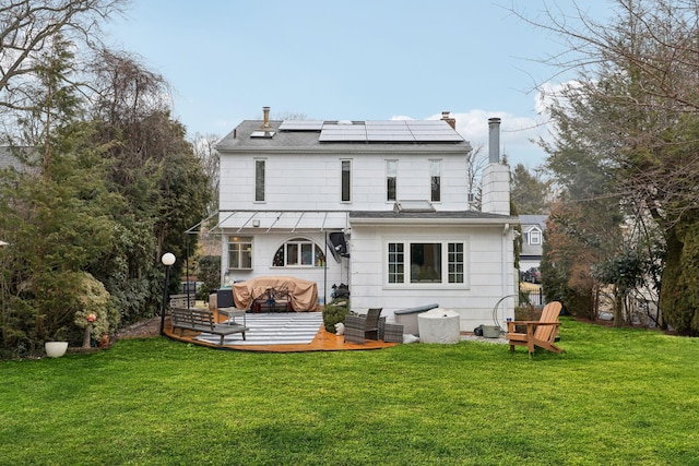 rear view of house with roof mounted solar panels, a lawn, an outdoor hangout area, and a chimney