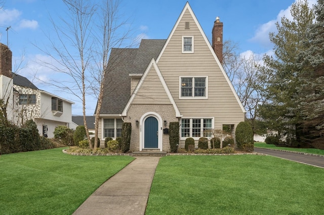 tudor house featuring a shingled roof, a chimney, and a front yard