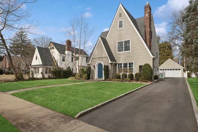 view of front of home featuring a chimney, a detached garage, roof with shingles, an outdoor structure, and a front yard