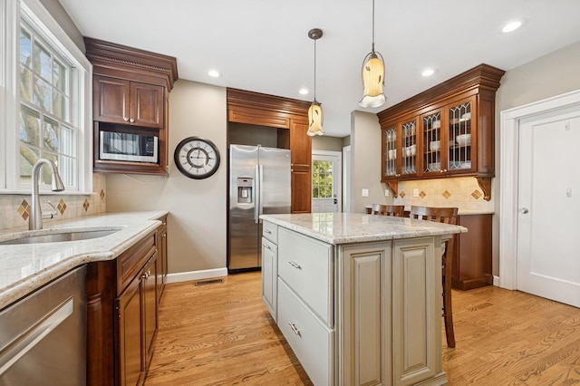 kitchen featuring light wood finished floors, glass insert cabinets, decorative light fixtures, stainless steel appliances, and a sink