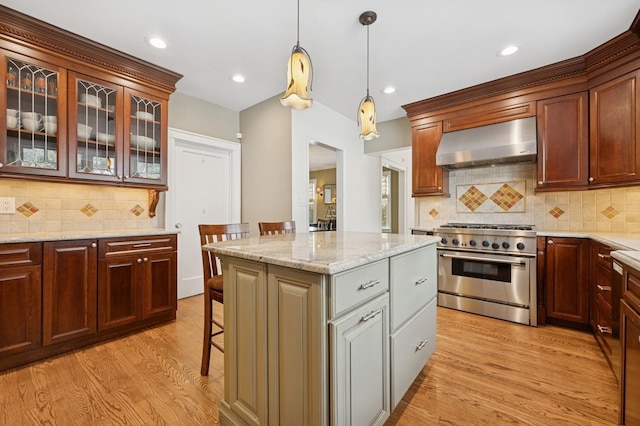 kitchen with pendant lighting, high end stainless steel range, a kitchen island, wall chimney range hood, and light wood-type flooring