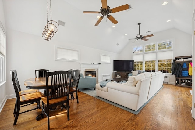 living room featuring visible vents, a glass covered fireplace, hardwood / wood-style floors, high vaulted ceiling, and recessed lighting