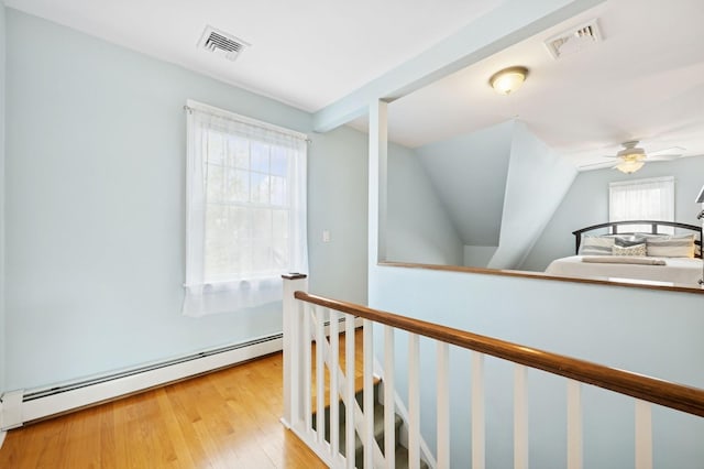 hall with a baseboard radiator, visible vents, wood finished floors, and an upstairs landing