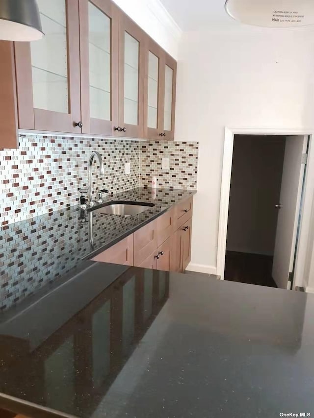 kitchen with decorative backsplash, glass insert cabinets, light brown cabinets, a sink, and dark stone countertops