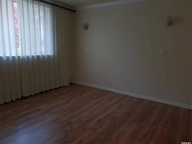 empty room with crown molding, baseboards, and wood finished floors